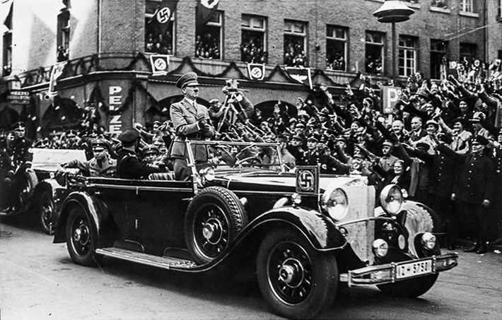 Hitler Archive | Adolf Hitler is standing in his open car while driving through Cologne